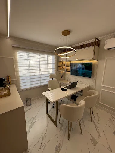 Consultório com mesa branca, notebook, persiana clara e luminária circular dourada